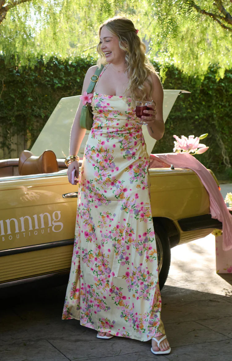 Yellow floral satin maxi dress with a cowl neck, spaghetti straps, and a ruched side detail