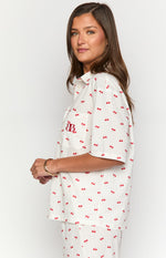 Side view of a white cherry print pajama shirt with short sleeves and a red embroidered logo on the pocket