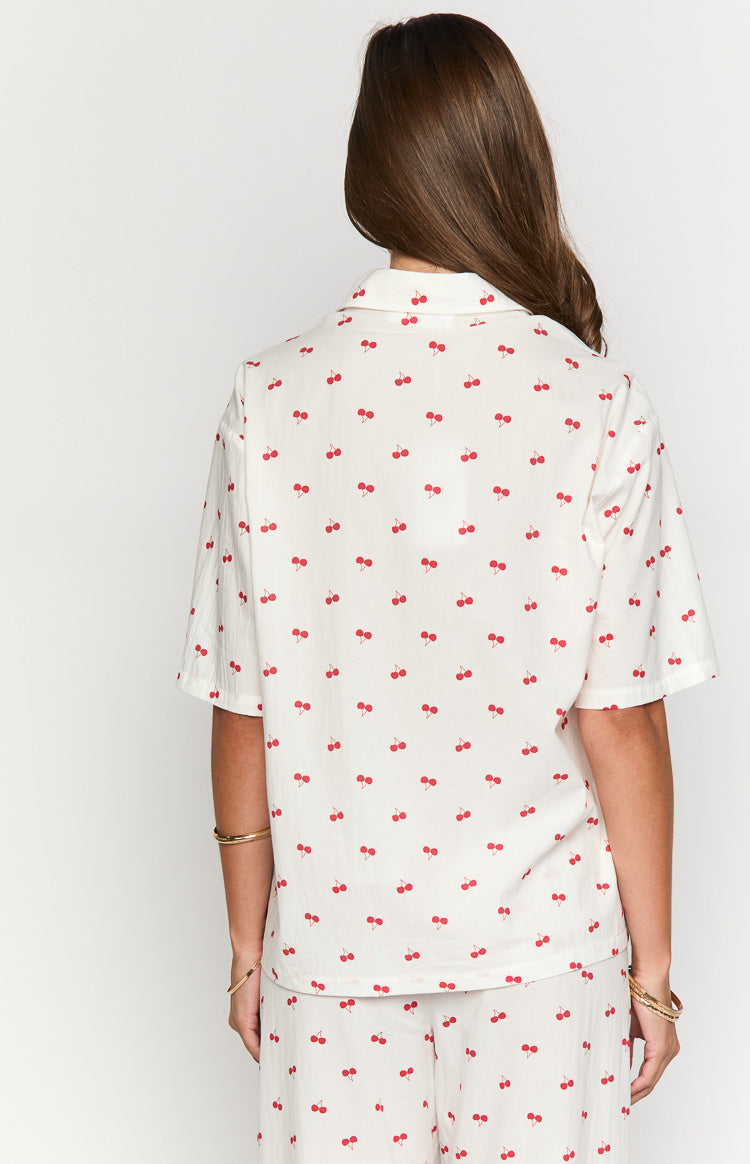 Rear view of an off-white pajama shirt with a red cherry print, featuring a collared back and short sleeves