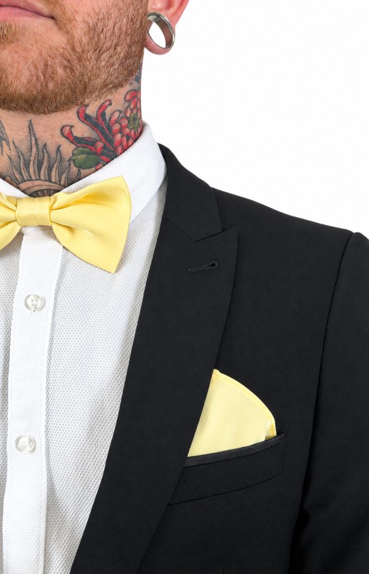 Close-up of a yellow bow tie and matching yellow pocket square worn with a white textured shirt and black suit jacket