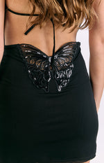 Close-up of the large black sequined butterfly detail on the sheer back of the black mini dress with halter ties