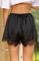 Rear view of black satin shorts with a gathered elastic waist and wide scalloped lace trim