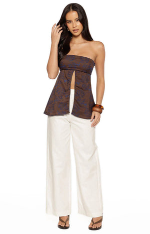 A lifestyle shot of our model wearing a strapless brown top. This top features a repetitive blue floral-line pattern and a unique open-front slit that starts at the high waist and extends to the bottom hem.