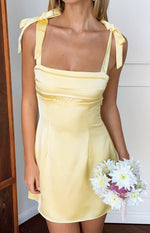 Close-up of a yellow satin mini dress with tie shoulder straps and a square neckline with horizontal bust panels