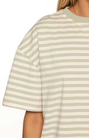 Close-up of our model wearing an oversized loose-fitting crew-neck t-shirt with a horizontal stripe pattern in alternating sage green and white. This top has short sleeves and a solid sage green collar trim.