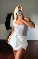 Front view of a white denim asymmetrical wrap mini skirt with a single button closure