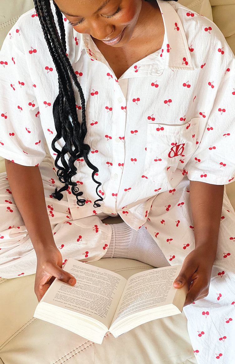 Close-up of the white cherry print pajama shirt with a red embroidered BB logo on the chest pocket and matching pajama pants