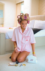 Light pink and white striped pajama shirt with a notched collar, short sleeves, red piping, and embroidered logo on the chest pocket