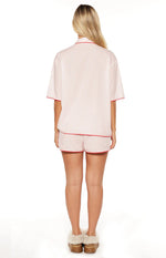 Rear view of a pink striped pajama shirt with short sleeves and matching shorts, both with red piping