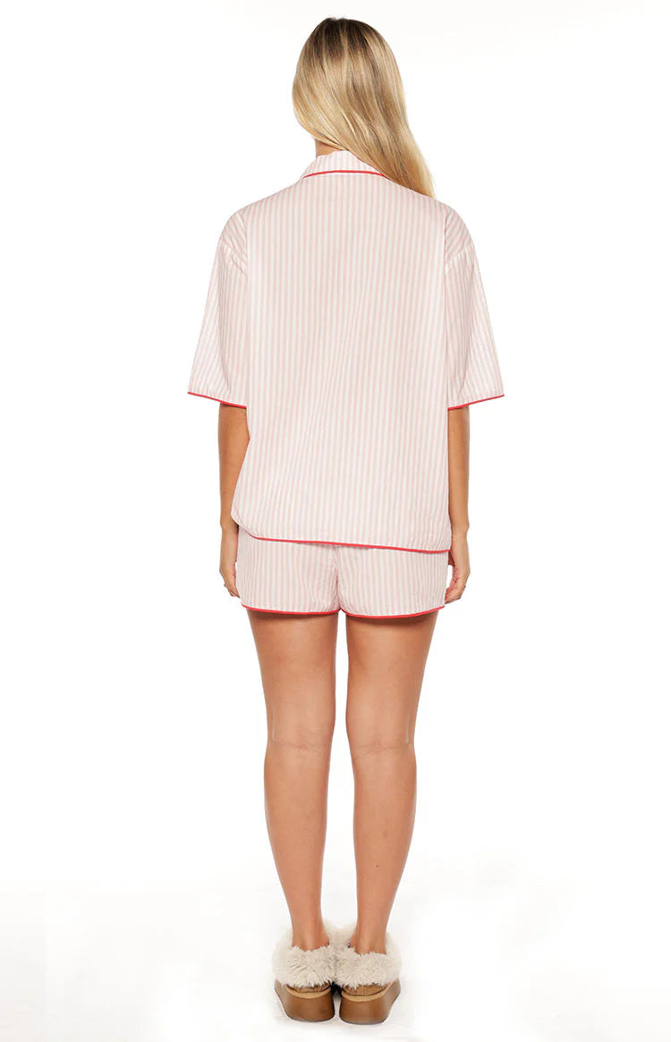 Rear view of a pink striped pajama shirt with short sleeves and matching shorts, both with red piping