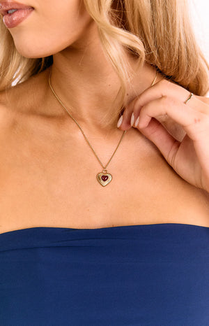 Close-up of a gold chain necklace with a red heart pendant featuring a textured gold border