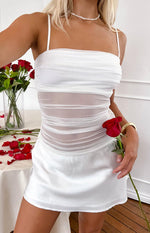 Close-up of a white mini dress with ruched mesh bodice, sheer midriff panel, and satin skirt