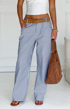 Model wears blue and white striped pants with a white top- brown belt- and matching handbag- showcasing stylish wide-leg trousers.