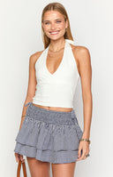 model wearing a white halter neck top wth cross over details at the bust paired with a mid wash denim mini skirt