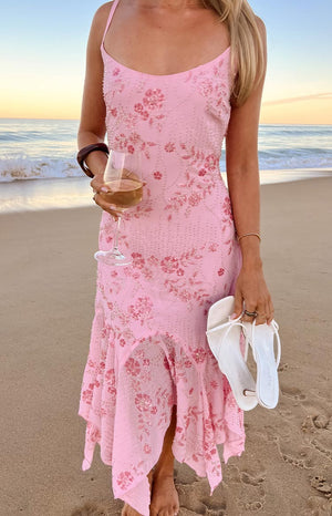 A sleeveless- pink floral-print midi-dress with a delicate floral pattern- a gathered waist- and an asymmetrical- handkerchief-style hemline. This dress is suitable for a beach wedding or a daytime party.