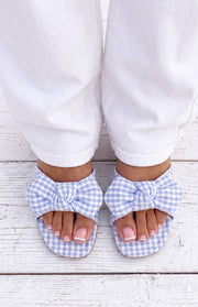 Overhead view of blue and white gingham check sandals with large fabric bows across the toes