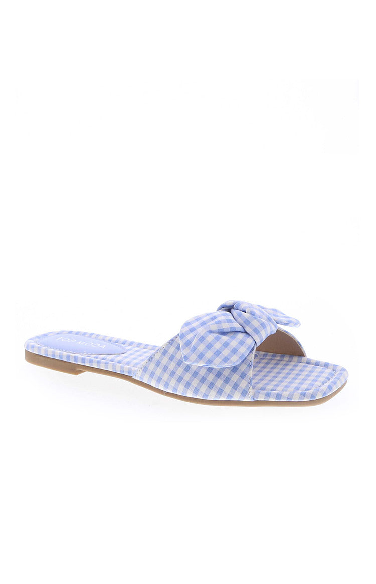 Side view of a blue and white gingham check slide sandal with a bow detail on the strap and a flat brown sole