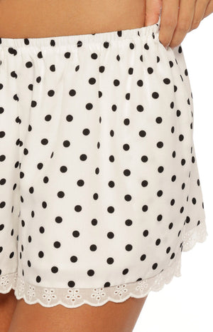 Close up of white shorts with black polka dots and a scalloped lace hemline styled with a matching top