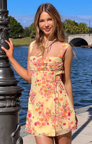 Girl in a casual yellow mini dress with a floral print and wide straps for a day event.