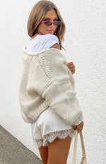 Rear-side view of a cream chunky knit cardigan with an oversized fit, dropped shoulders, and visible texture