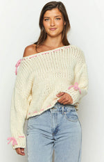 Rear view of a cream chunky knit sweater with pink lacing detail on the off-shoulder neckline, sleeves, and hem