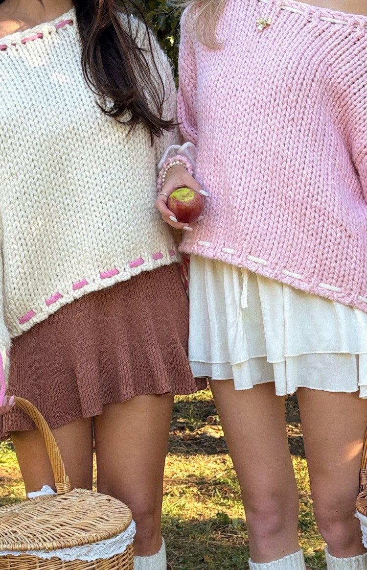 Chunky knit baby pink sweater with white stitched detail at the neckline and an uneven hem