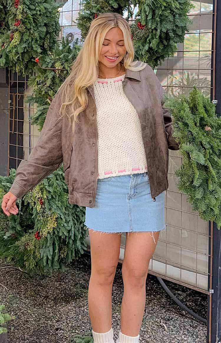 Rear view of a cream chunky knit off-shoulder sweater with pink stitching detail along the hem and pink ties on the sleeves