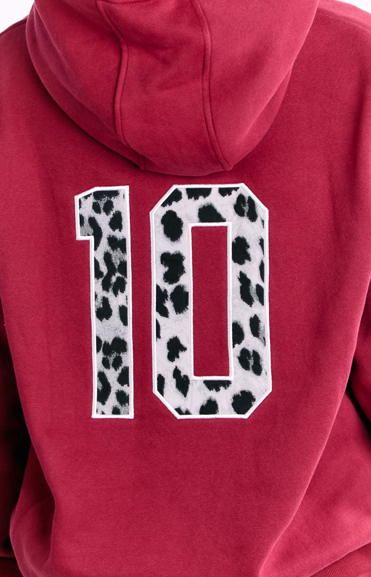 The back of a red hooded sweatshirt featuring a large number 10 applique with a black and white cow print pattern.