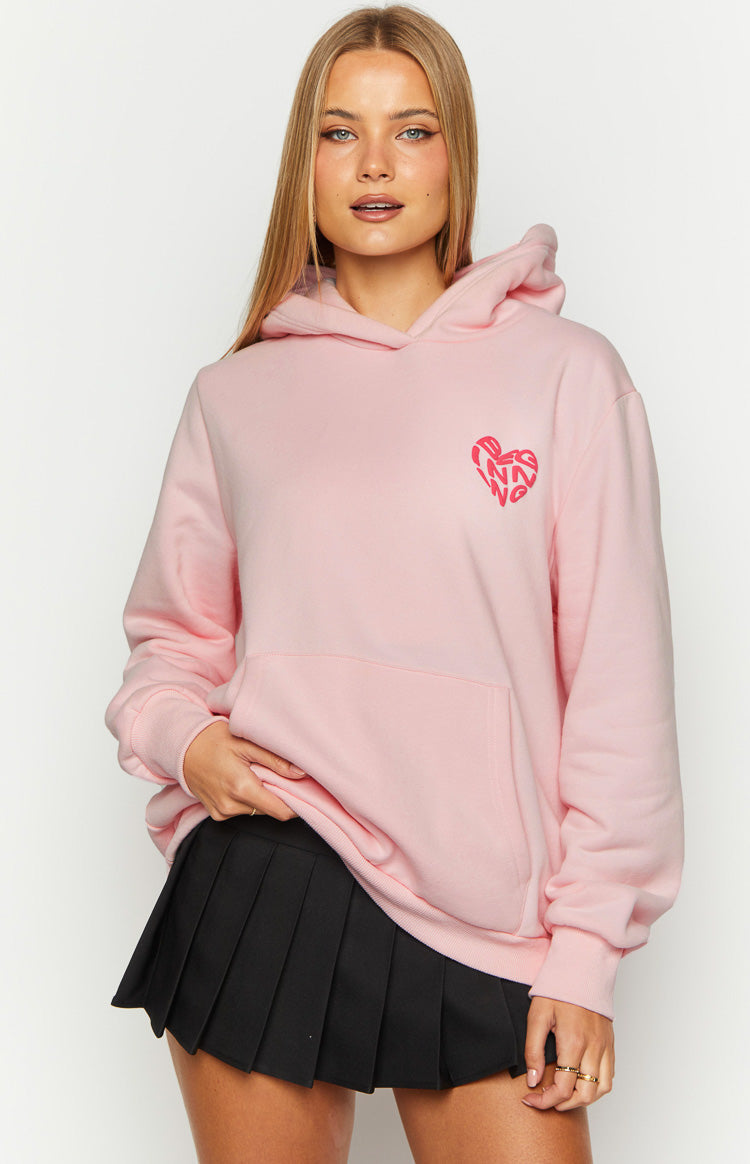 Front view of a pink hoodie with a small heart graphic on the left chest, featuring a kangaroo pocket and ribbed cuffs