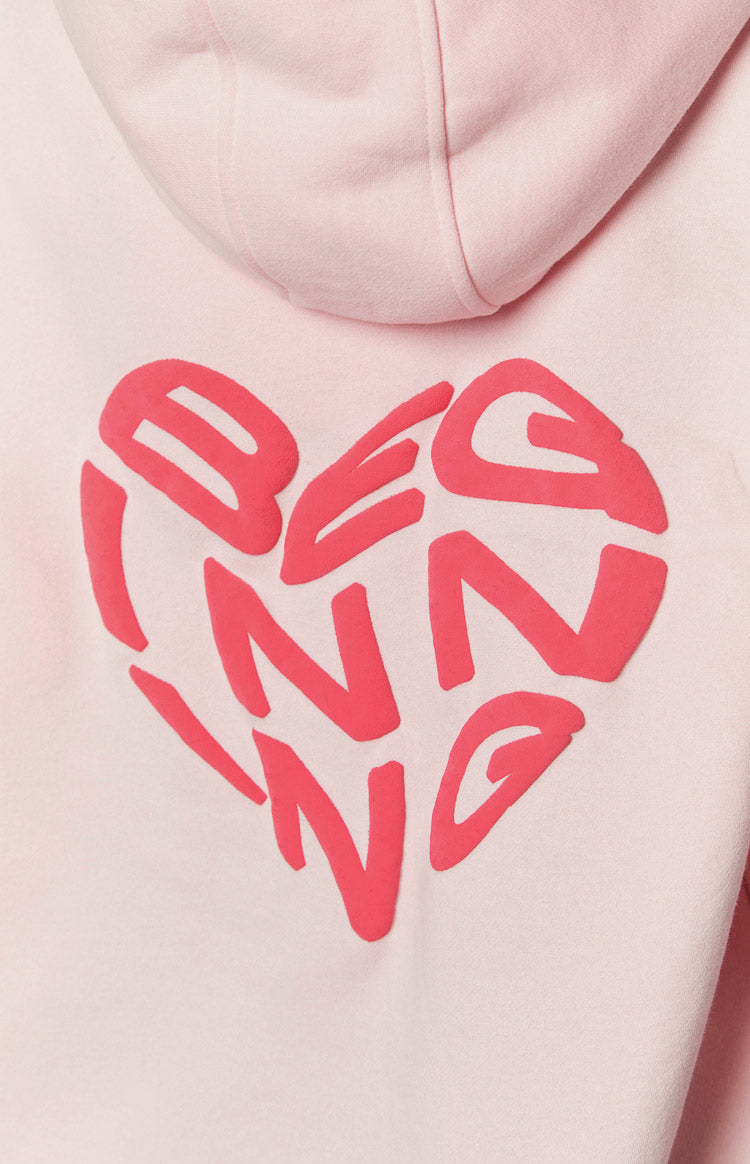 Close-up of the back of a pink hoodie showing a raised red heart graphic with "BEGINNING" text inside