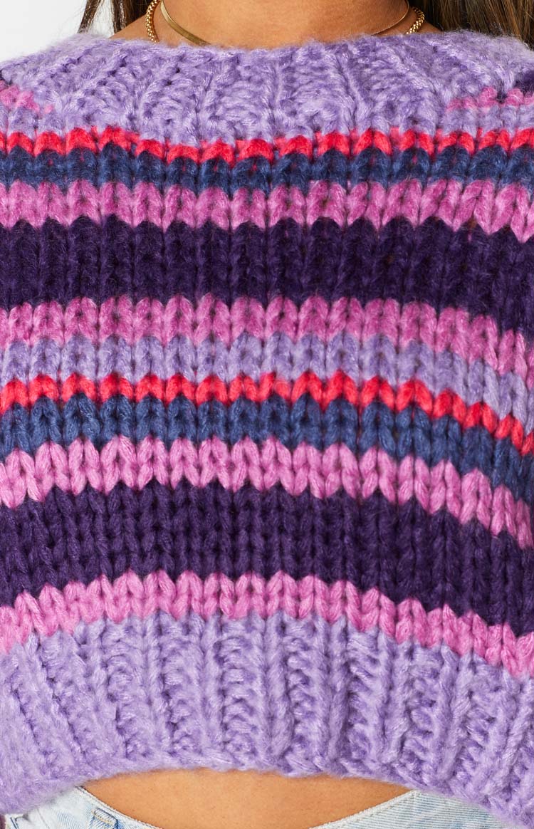 Chunky knit purple sweater with ribbed round neckline and horizontal stripes in dark purple, light purple, pink, and red