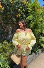 Yellow Bardot mini dress with a ruffled off-shoulder neckline, front tie detail, long billowy sleeves, and elasticated waist