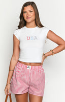 Model is wearing red and white vertically striped boxer-style shorts with an elasticated waistband. The shorts are paired with a white ribbed cropped tank top that has an American flag embroidery.