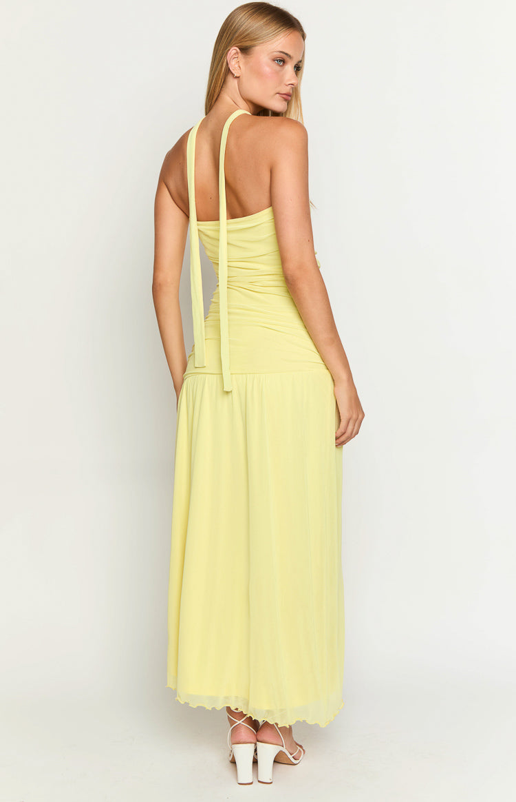 Rear view of a yellow maxi dress showing the halter neck ties, ruched bodice, flowy skirt, and scalloped hem