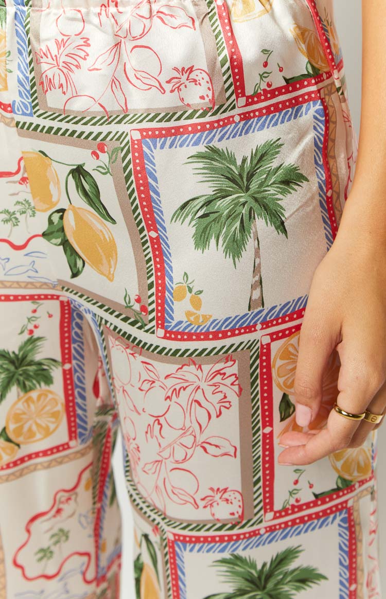 Close-up of the white satin pants with a colorful Roma print featuring palm trees, lemons, and strawberries in bordered squares
