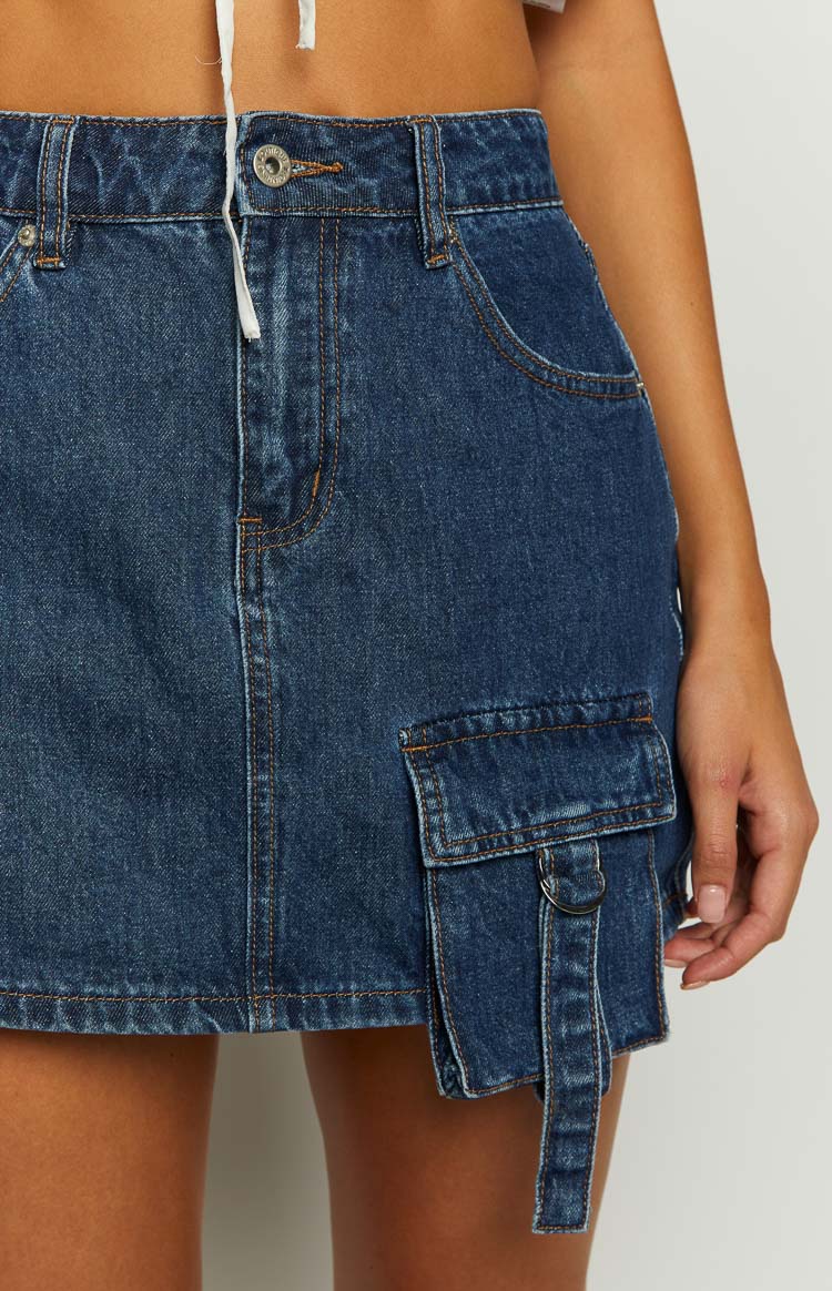 Close-up of the dark wash denim mini skirt showing the front cargo pocket with strap and D-ring