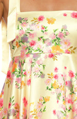 Close-up of the yellow satin mini dress with a vibrant floral print of pink, orange, and purple flowers, green leaves, and tie straps