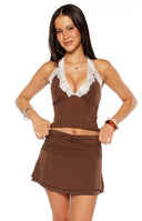 Our model wearing a brown halter top with a small white polka dot pattern featuring a plunging V-neckline trimmed with white floral lace.