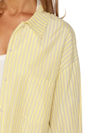 Girl sitting in a relaxed yellow striped long sleeve shirt with cuffs unbuttoned ideal for a laid back Brunch look