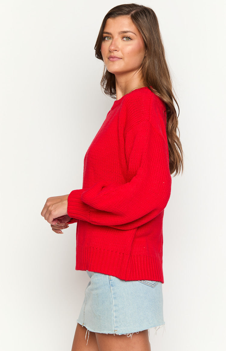 Side view of a red knit sweater with ribbed cuffs and a textured hem detail