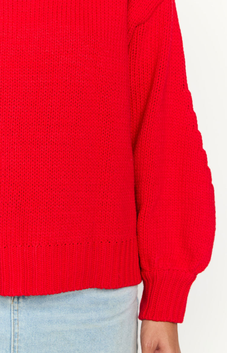 Close-up of the red chunky knit sweater showing the ribbed hem and the long puffed sleeve with a ribbed cuff