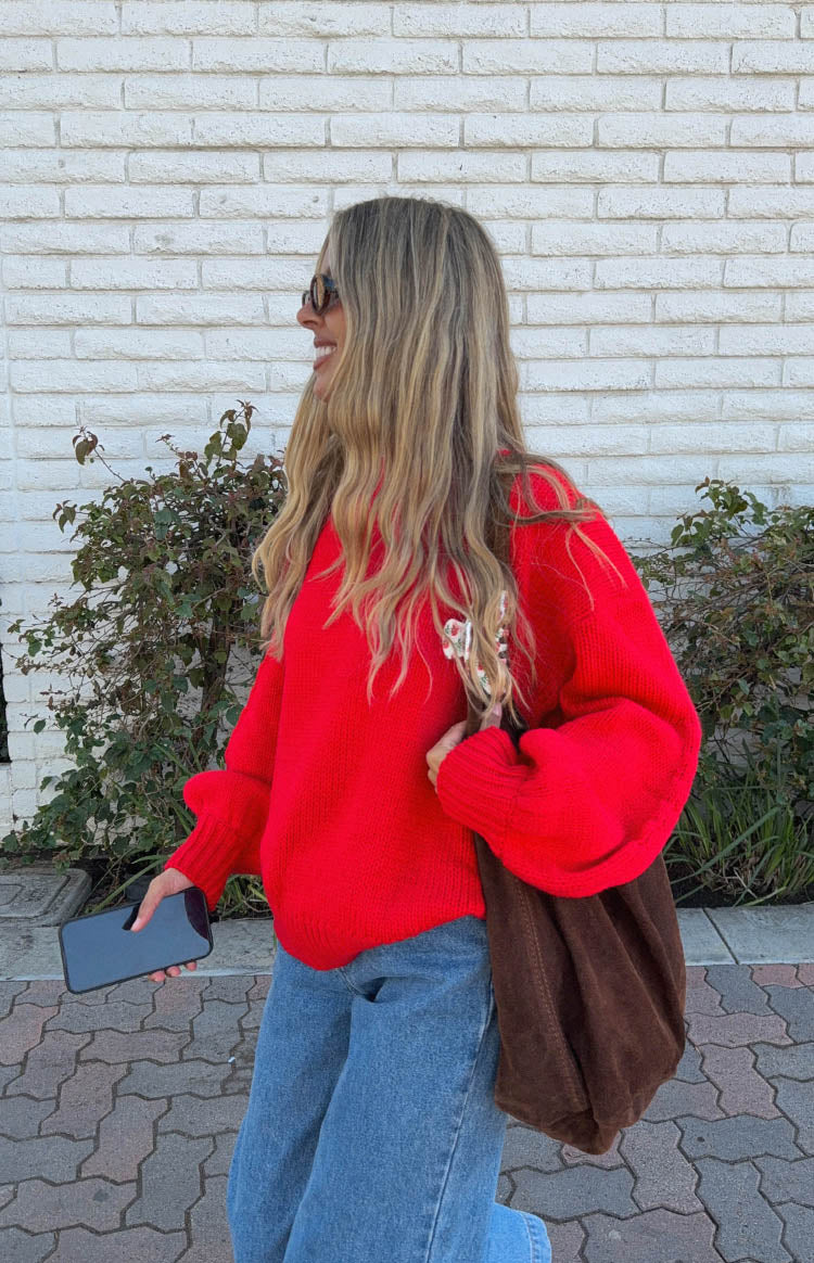 Side view of a red oversized knit sweater with voluminous long sleeves, ribbed cuffs, and subtle floral embroidery