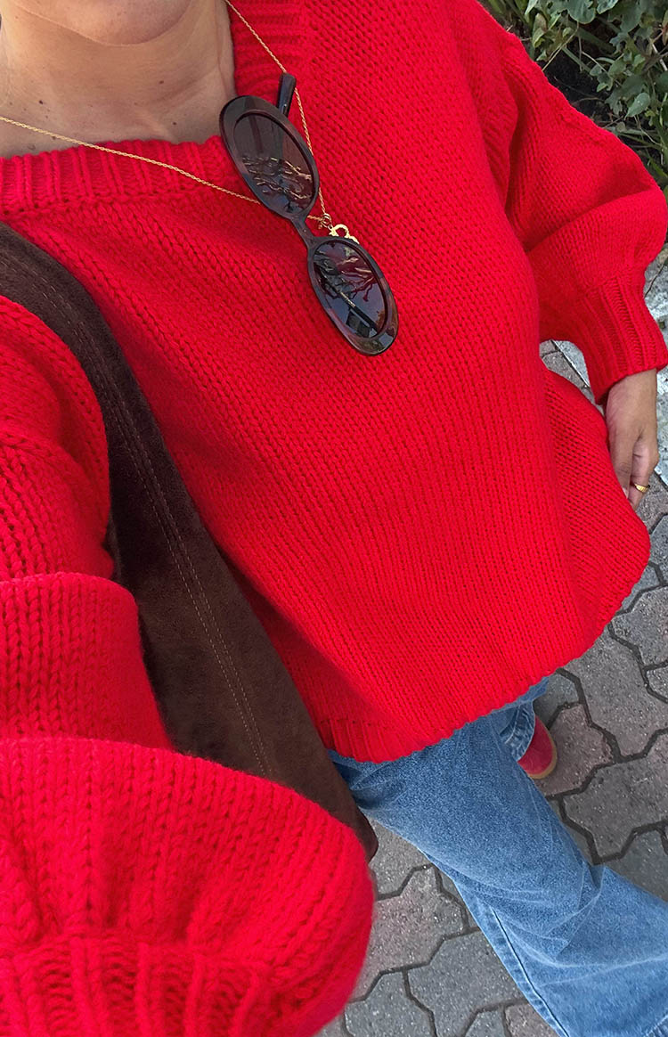 Close-up of the chunky knit texture and relaxed fit of a red boat neck sweater with wide sleeves