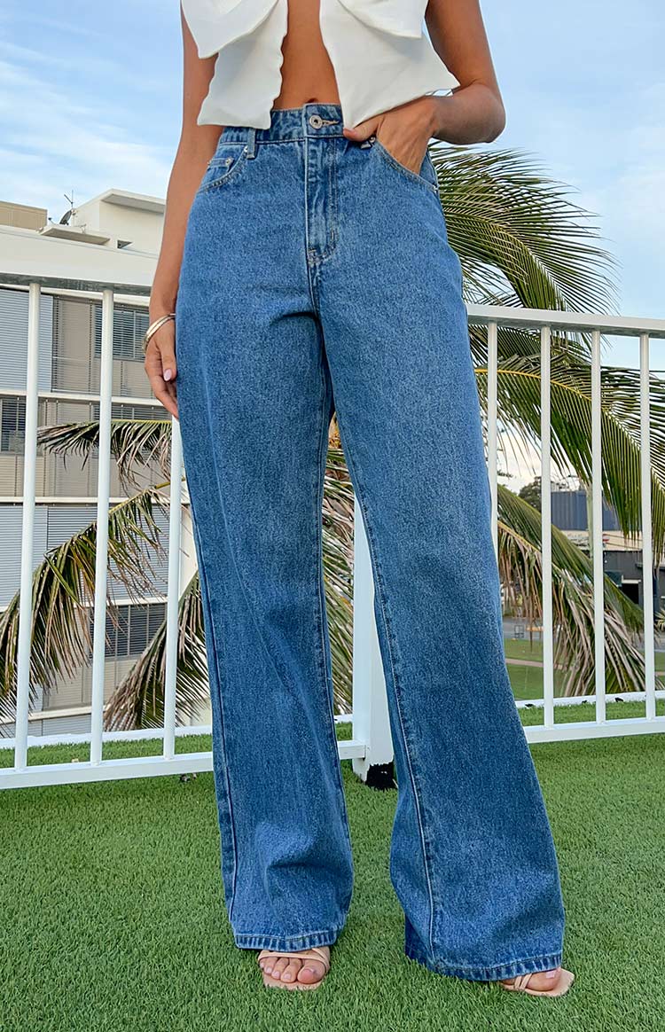 Full length view of mid-wash blue denim slouchy jeans with a mid-rise waist and wide leg, hand in pocket