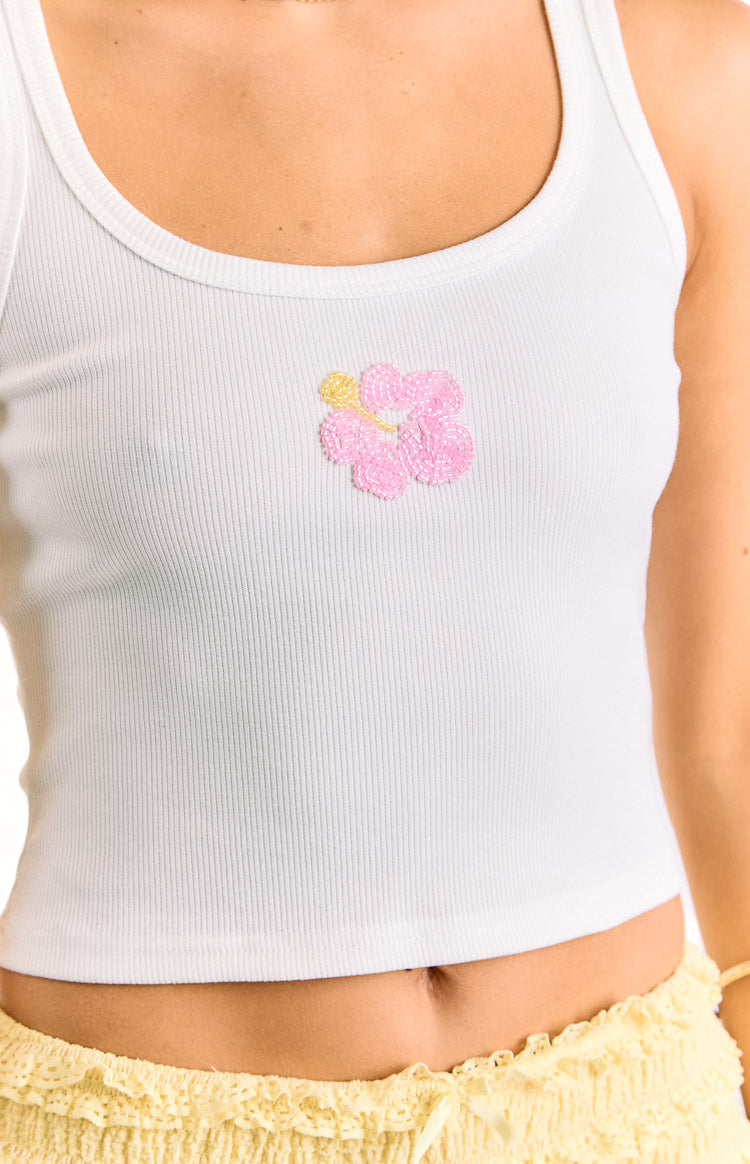 Close-up of the pink beaded hibiscus detail on the chest of a white ribbed scoop neck tank top