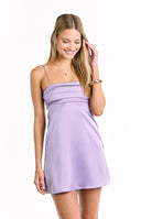 A short- sleeveless mini-dress in a light lavender color- featuring thin spaghetti straps and a ruched or pleated horizontal detail across the bust. This dress is suitable for a semi-formal summer day or a party.
