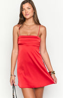 Model posing in a vibrant red satin mini dress suitable for homecoming. The dress features a straight- ruched neckline and thin spaghetti straps for a chic- formal look.