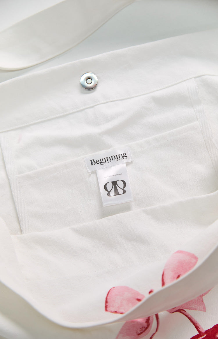 Close-up of the white tote bag featuring a red cherry graphic with pink bow and 'Beginning' text