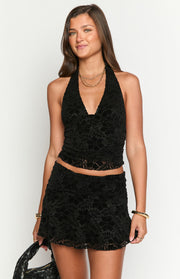 Close-up front view of a black velvet halter crop top with a deep V-neck and floral pattern