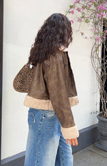 Side view of a distressed brown aviator jacket with cream sherpa lining at the cropped hem and cuffs